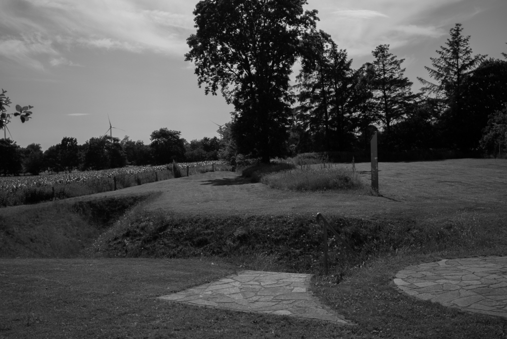 Ehemaliger Panzergraben (Bild vorne links), im Bild rechts die Stahl-Stele „Das Mal“ 